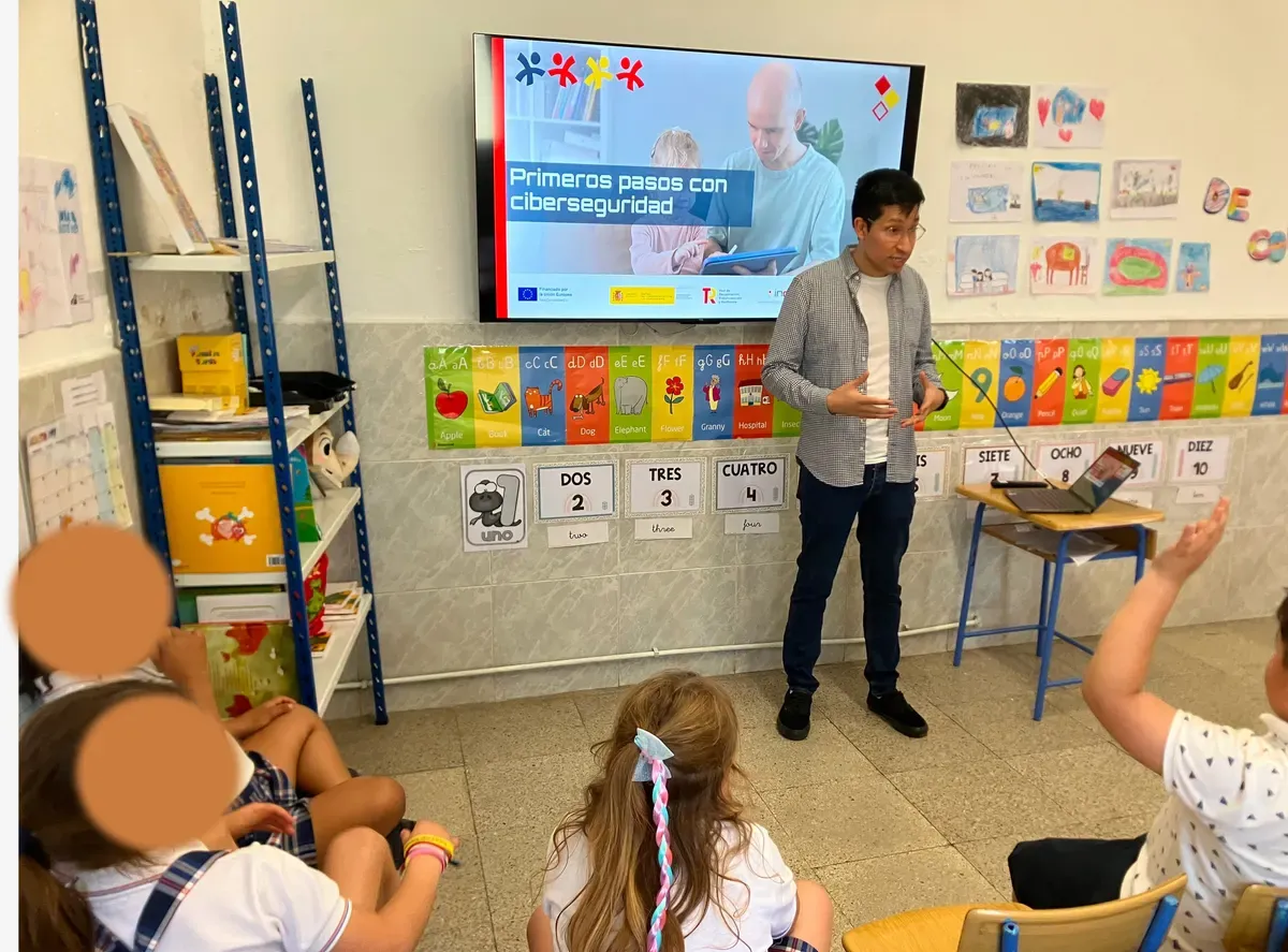 Bray Lozano gives a talk in a primary school classroom in front of the title slide of INCIBE's Primeros pasos con ciberseguridad, while a girl raises her hand