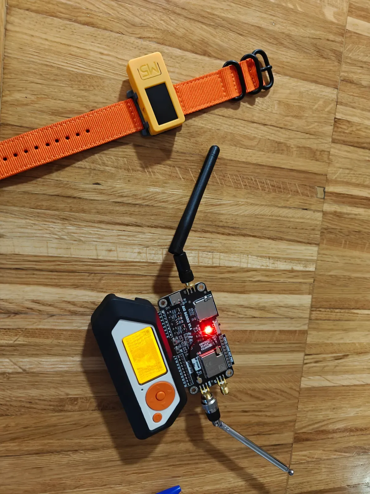Ethical hacking kit on a table: a board with an antenna, a pocket analyser and a wrist device with a screen