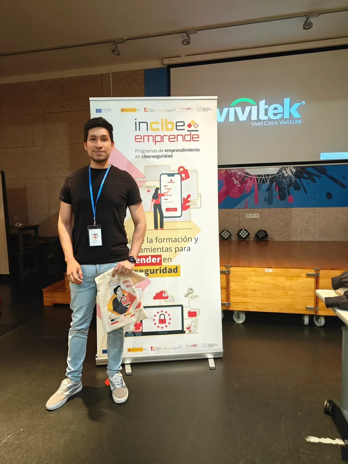 Bray Lozano next to the INCIBE Emprende programme banner, holding the workshop material